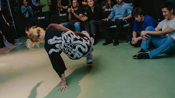 Person breakdancet drinnen, Zuschauer umher.