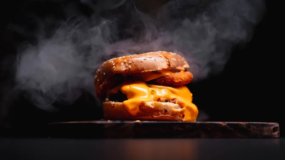 Cheeseburger steaming on wooden board.