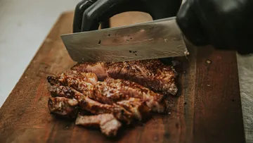 Behandschuhte Hände schneiden Steak auf Schneidebrett.