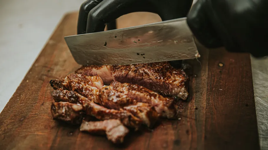 Behandschuhte Hände schneiden Steak auf Schneidebrett.