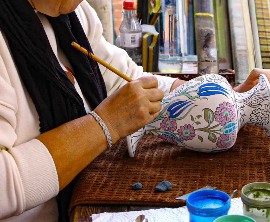 Person malt Blumendesign auf Vase.