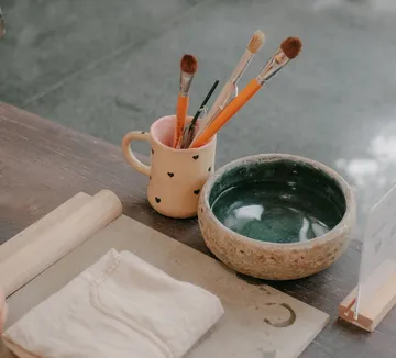 Paintbrushes in mug, near ceramic bowl.