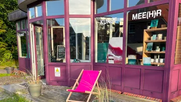 Gallery with artworks and pink chair outside.