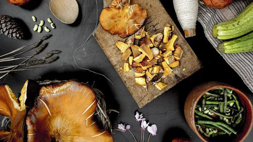 Chopped wild mushrooms on wooden board surrounded by vegetables.