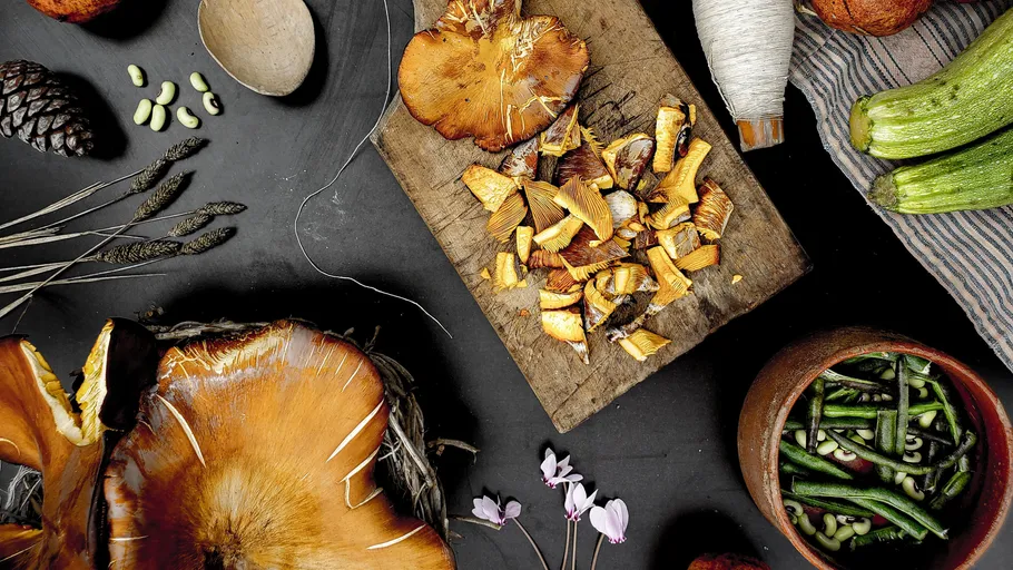 Chopped wild mushrooms on wooden board surrounded by vegetables.