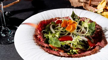 Plate of carpaccio with salad garnish.