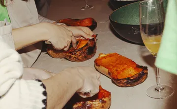 Hands preparing roasted squash on table.