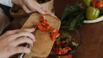 Hands chopping tomatoes on wooden board.