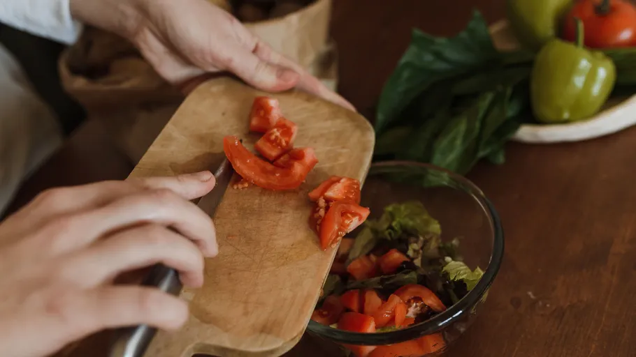 Hands chopping tomatoes on wooden board.