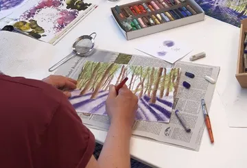 Person drawing pastel artwork on table.