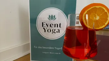 Getränk mit Orangenscheibe neben Event-Poster.