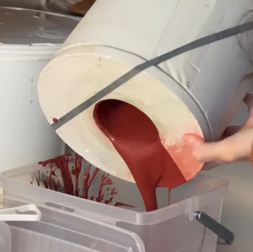 Behälter gießt rote Flüssigkeit in Plastikbehälter.