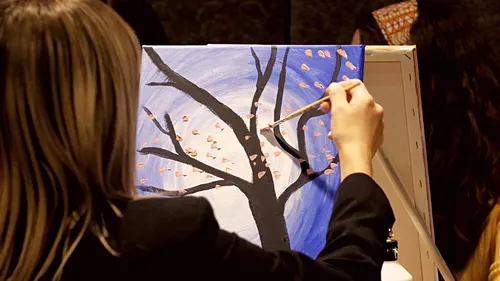 Person painting tree on canvas indoors.