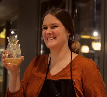 Frau hält Getränk, lächelt drinnen.