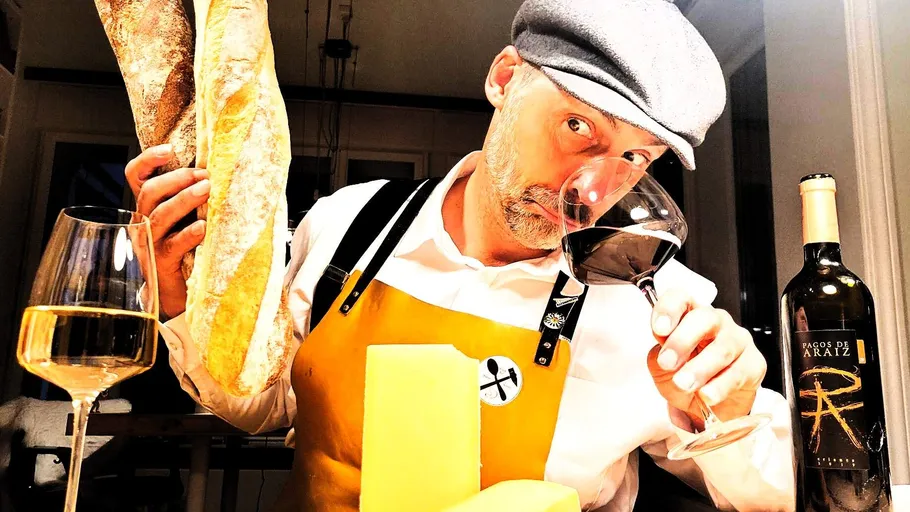 Man in apron holding bread, sniffing wine.