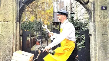 Mann mit Schraubenschlüssel fährt Rad durch Tor.