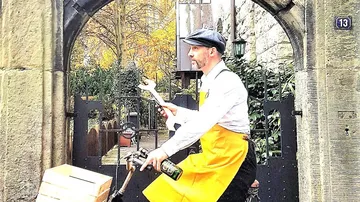 Mann radelt mit Schraubenschlüssel, Hof im Hintergrund.