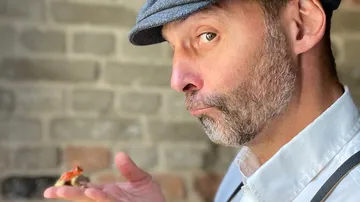 Man holding a tiny red dinosaur indoors.