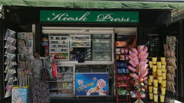 Person kauft an Kiosk mit Zeitungen.