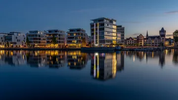 Gebäude spiegeln sich im Wasser bei Dämmerung.