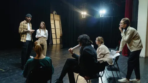 Schauspieler proben Drehbuch auf Bühne, gedämpft beleuchtet.
