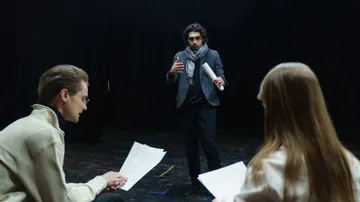 Person coaching actors on dark stage.