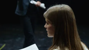 Frau hält Papier, dunkler Hintergrund.