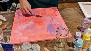 Person painting red canvas with knife.