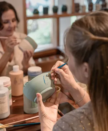 Person painting pottery in art studio.