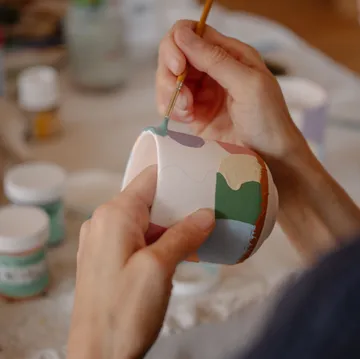 Hands painting ceramic cup on table.