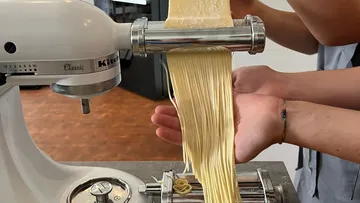 Hands guiding pasta through a pasta roller.
