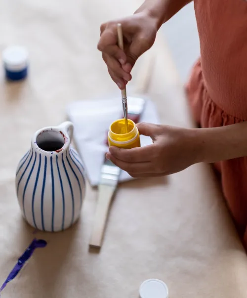 Hands mixing yellow paint with brush.