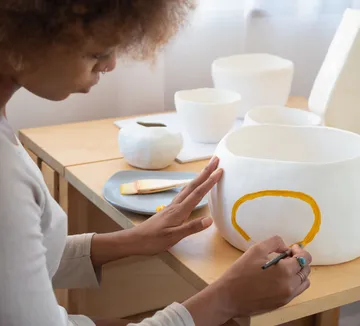 Person painting pottery on a table.