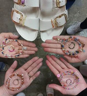 Hands holding beaded bracelets near sandals.