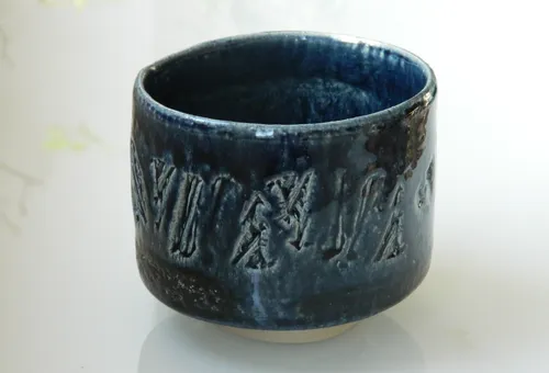 Keramikbecher mit Gravuren auf weißer Fläche.
