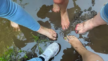 Füße im Schlamm nahe flachem Wasser.