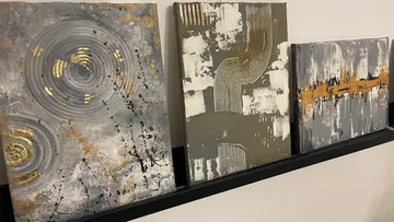 Drei Gemälde hängen an einer Wand auf einem Regal.