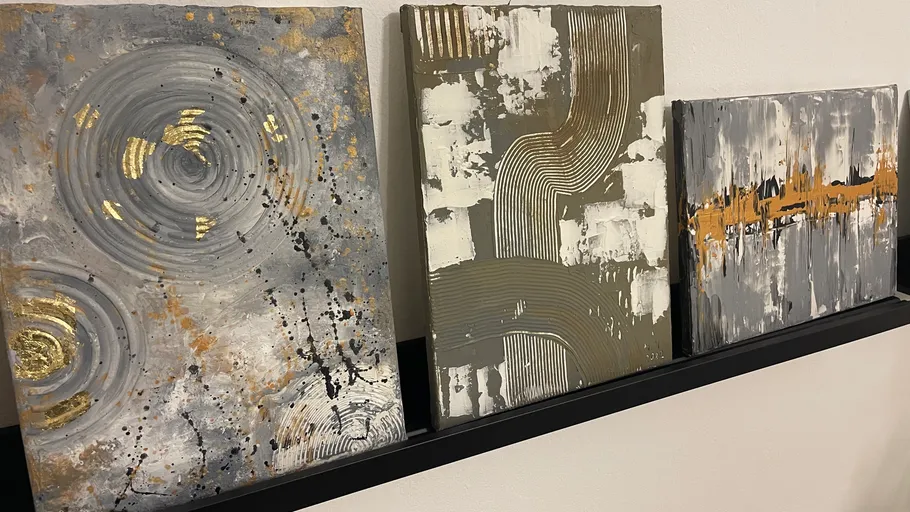 Three paintings hang on a wall on a shelf.