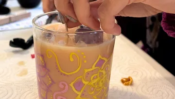 Hand fügt Eis in verziertes Getränkeglas.