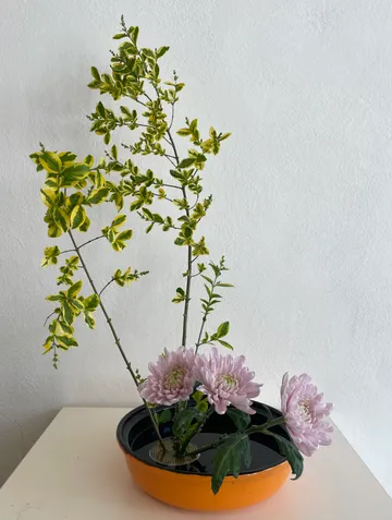 Flower arrangement in a shallow orange bowl.