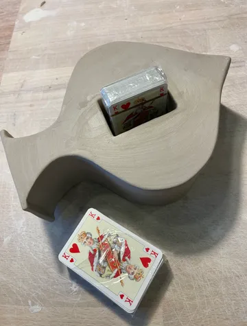Tonskulptur hält Kartendeck, Holztisch.