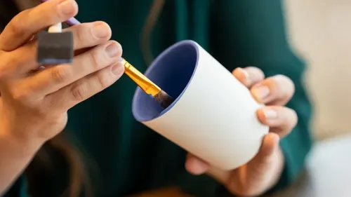Hände bemalen eine Keramiktasse drinnen.