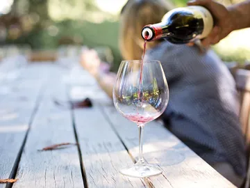 Red wine is poured into a wine glass on a table.