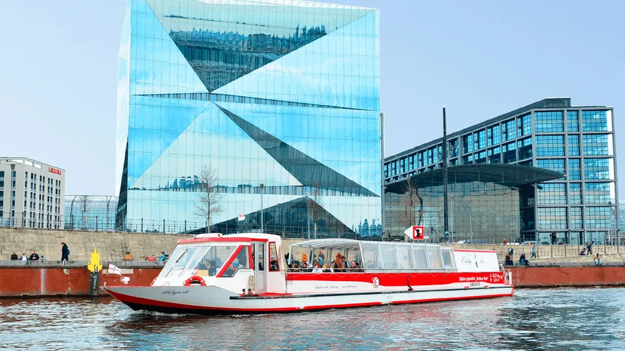 Boat cruising on river beside modern buildings.