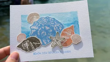 Hand hält Karte mit Muscheldesign.