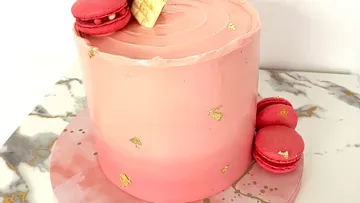 Pink cake with gold accents, macarons on top.