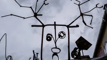 Metallskulptur in Form eines Gesichts vor Wolken.