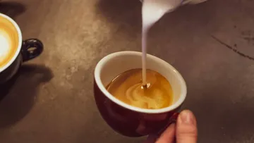 Kaffeetasse, in die Milch gegossen wird.