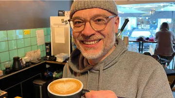 Mann hält Latte an Cafétresen.
