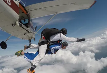 Tandem-Fallschirmspringer springen aus Flugzeug über Wolken.